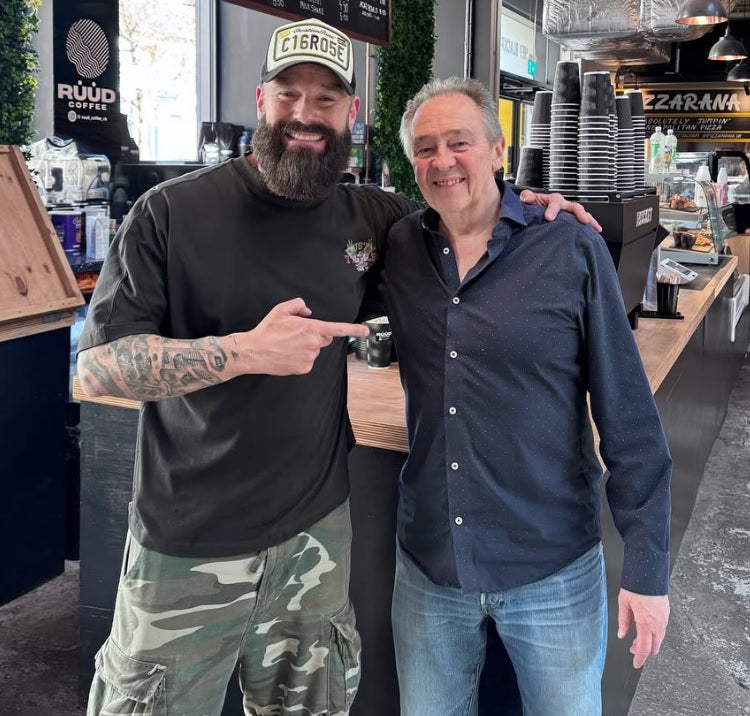 Two men posing together in a casual setting, possibly a bar or restaurant.